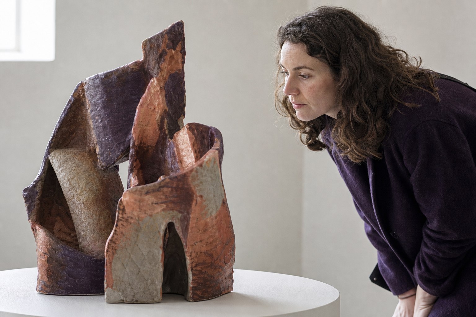Bezoeker bekijkt van dichtbij een abstract keramisch kunstwerk in een lichte galerie